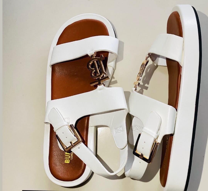 Women's sandals are white with a decorative buckle and logo, on a brown sole with black edging.